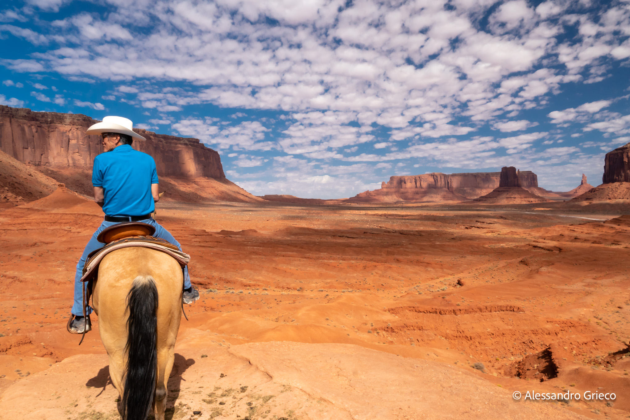 A rider crosses the valley floor below the Mittens, small as a thought